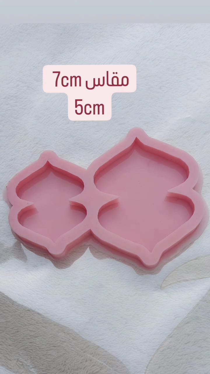 A silicone mold with two separate cavities, each shaped like a symmetrical arch or dome with pointed corners at the top and bottom. It is used for casting resin, wax, or ceramics, and can be used to make medals, car charms, earrings, or decorative items.