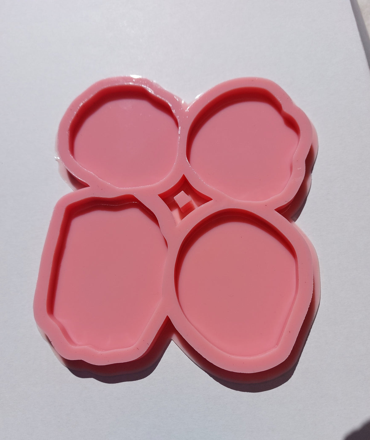 The silicone mold is divided into four separate cavities, each with a unique shape resembling natural stones with slightly wavy edges and varying sizes. It is used for casting resin, wax, or pottery