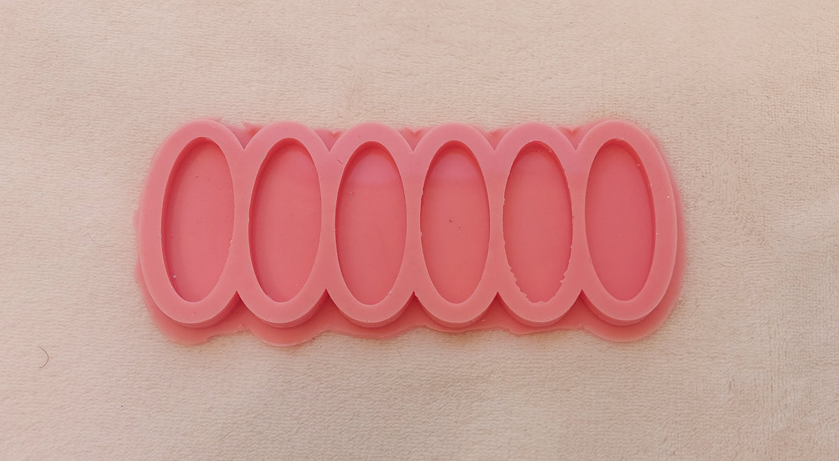 This silicone mold has six vertically aligned, elongated cavities. It is a common tool for casting resin or polymer clay to produce small, uniform decorative pieces. Dimensions: 2.5 x 5 cm, Depth: 6 mm