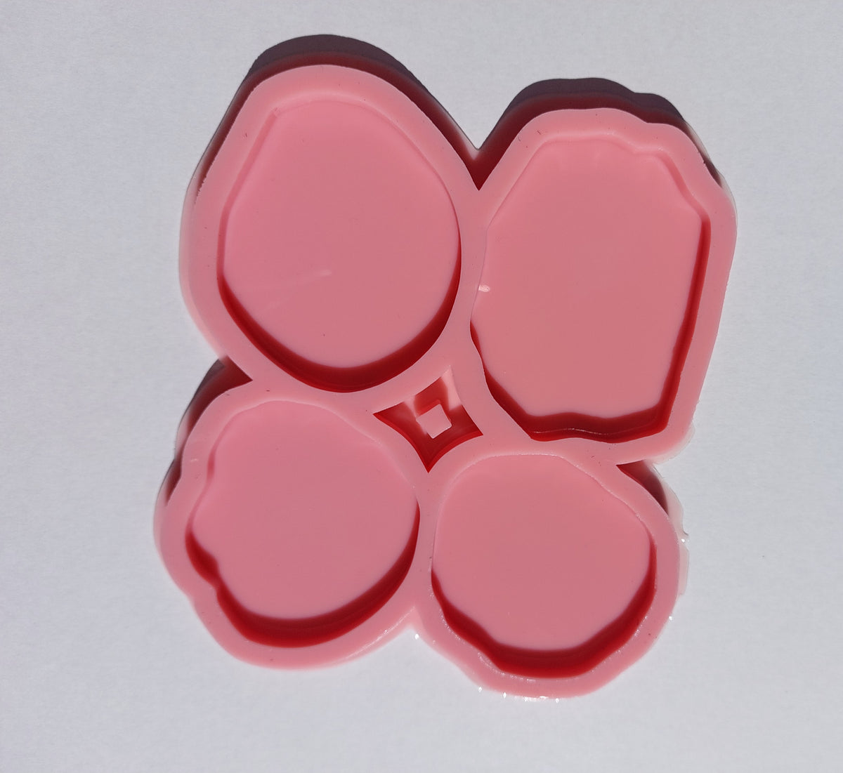 The silicone mold is divided into four separate cavities, each with a unique shape resembling natural stones with slightly wavy edges and varying sizes. It is used for casting resin, wax, or pottery