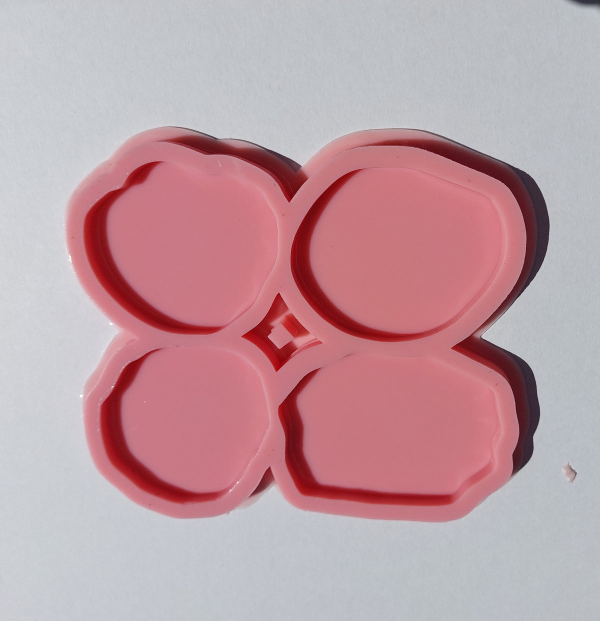 The silicone mold is divided into four separate cavities, each with a unique shape resembling natural stones with slightly wavy edges and varying sizes. It is used for casting resin, wax, or pottery