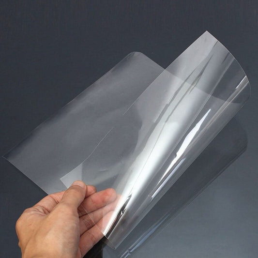 A flexible, transparent sheet made of plastic, often PVC, PET, or acetate, held in the hand to demonstrate its transparency and flexibility.