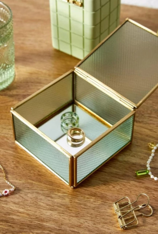 An antique glass jewelry box with a gold metal frame and mirror base that combines classic vintage style with elegant modern touches, making it a decorative piece in itself as well as a practical container for precious items