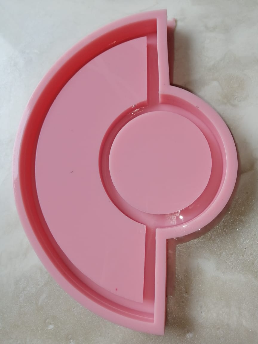 A silicone mold consists of a main cavity in the shape of a semicircle surrounding a complete circle in the center, with straight dividers separating the parts. It is used for casting resin, wax, or ceramics.