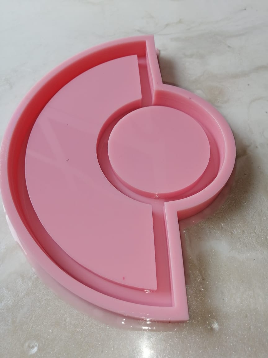 A silicone mold consists of a main cavity in the shape of a semicircle surrounding a complete circle in the center, with straight dividers separating the parts. It is used for casting resin, wax, or ceramics.