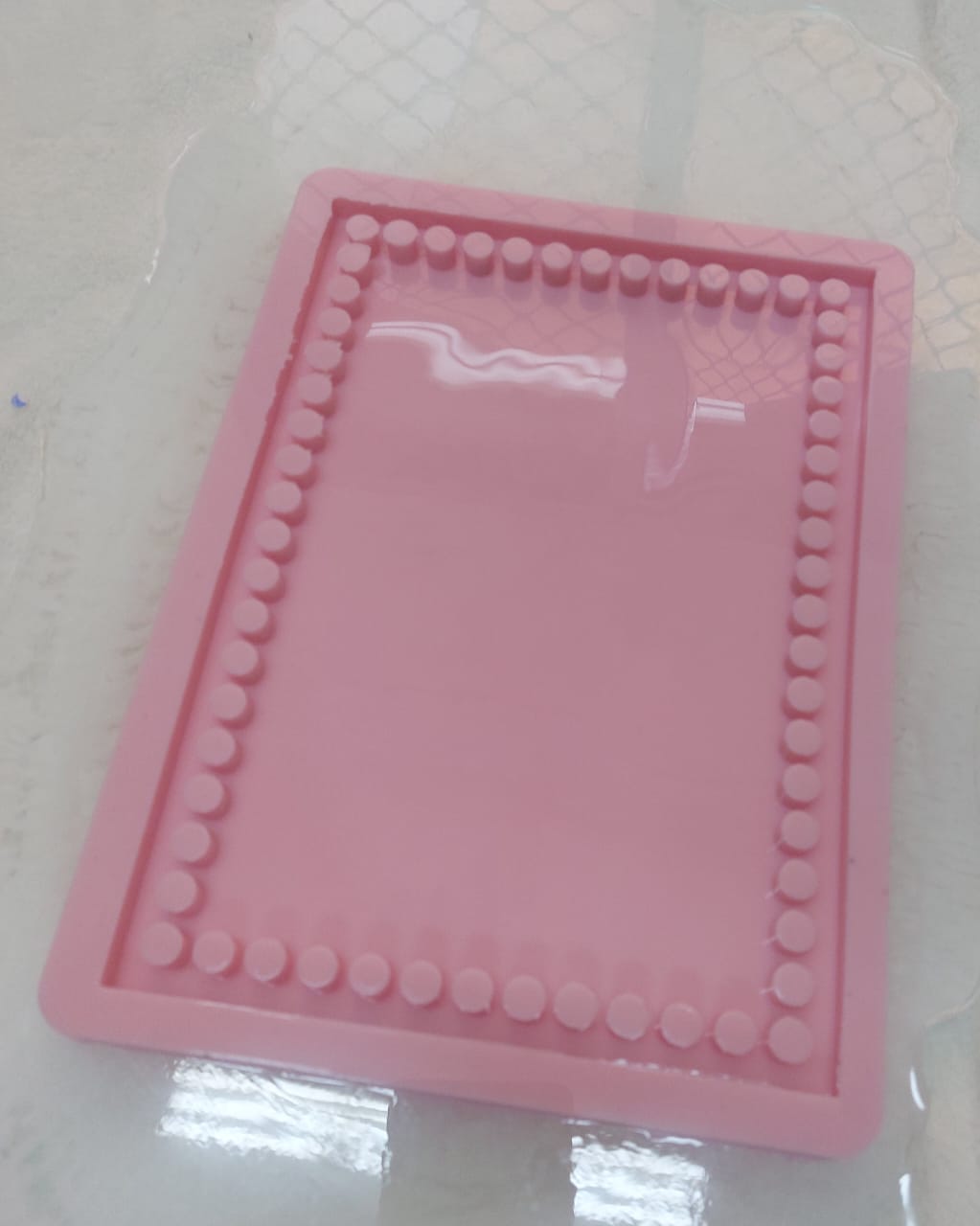 A light pink silicone mold featuring a unique design with an inner frame of small raised circles surrounding the flat area in the center. Length: 22 cm, Width: 16 cm, Depth: 8 mm