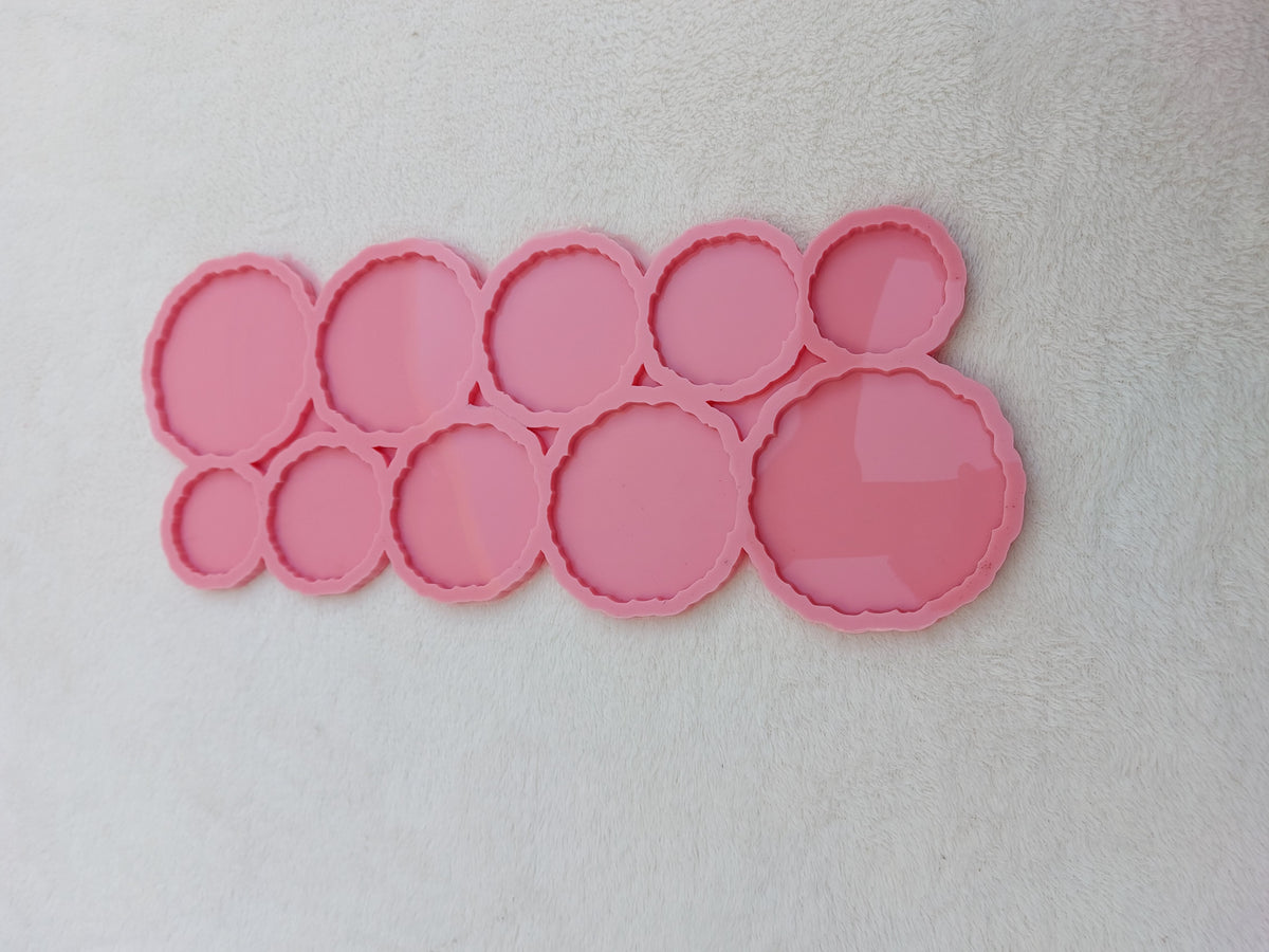 A silicone mold containing 10 interconnected circular cavities. The edges of all the circles feature a zigzag or wavy design in one piece. The cavities come in varying sizes and different diameters.