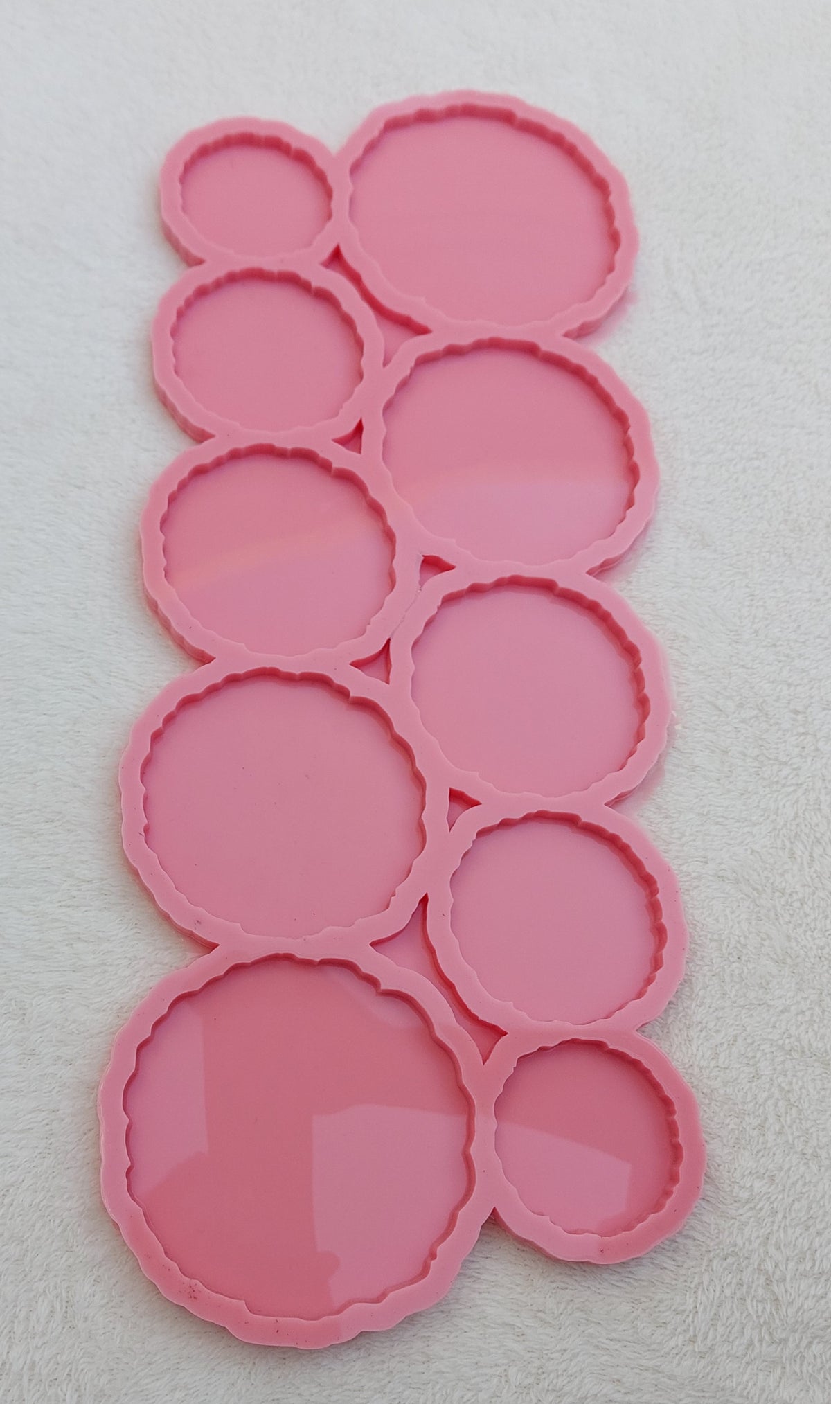 A silicone mold containing 10 interconnected circular cavities. The edges of all the circles feature a zigzag or wavy design in one piece. The cavities come in varying sizes and different diameters.