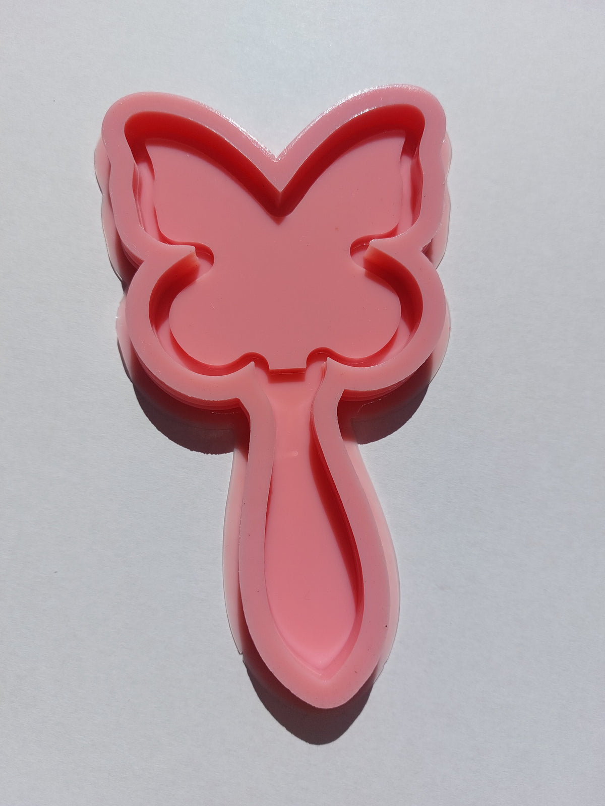A silicone mold designed in the shape of a large butterfly at the top, with a long, wide handle attached to its body at the bottom, creating a finished shape resembling a hand mirror. It is used for casting resin, wax, or pottery.